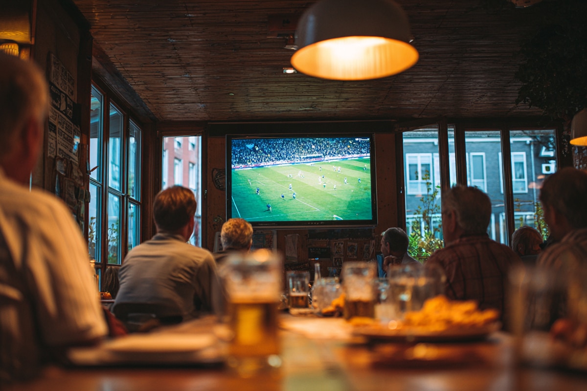 Amateurverein beim Public Viewing der WM 2026 im Vereinsheim, Mitglieder verfolgen das Spiel, Tippliste an der Holzwand
